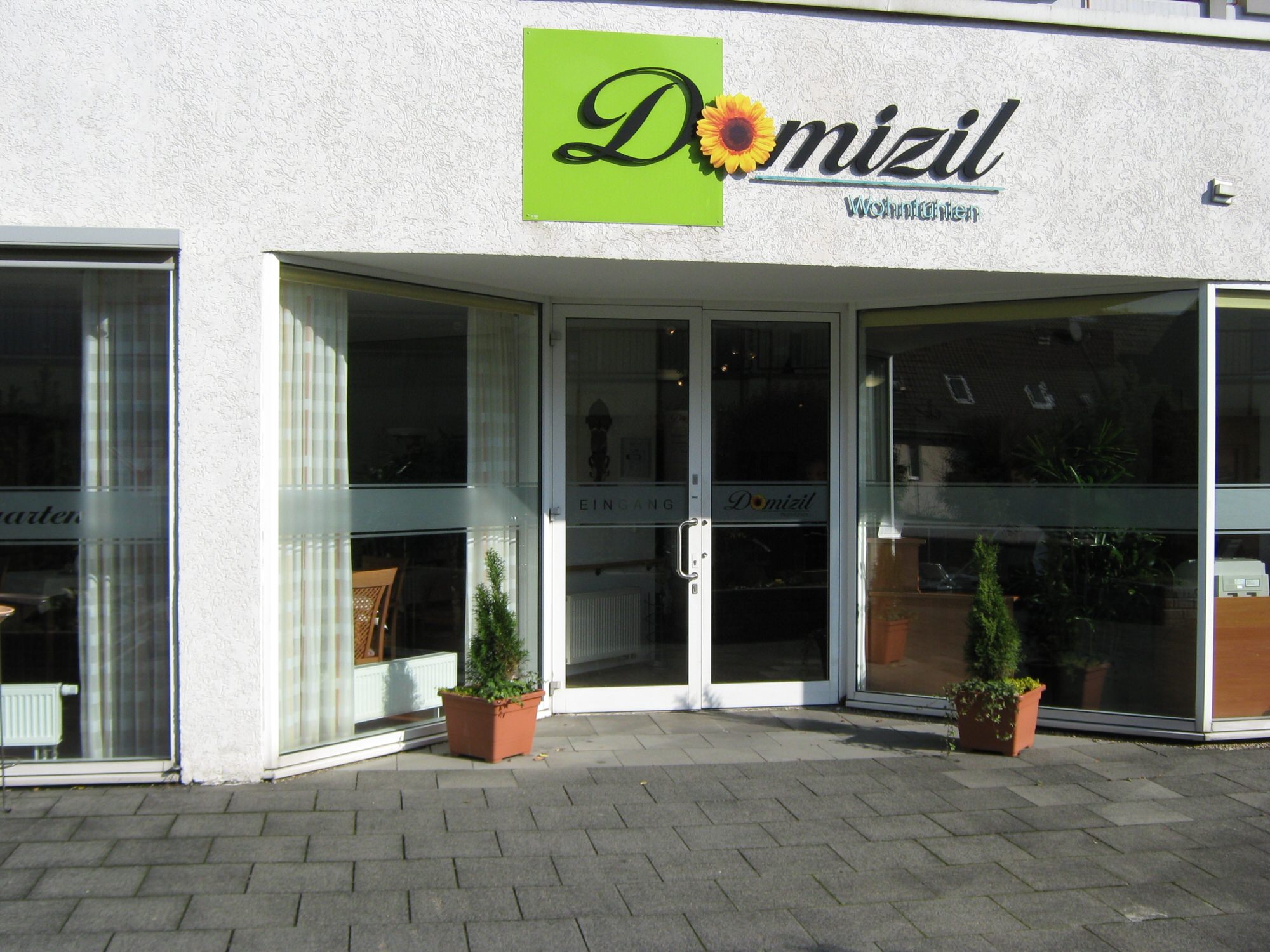Hauseingang des Domizil Wohnheims mit Glasfront und grünem Logo mit Sonnenblume.