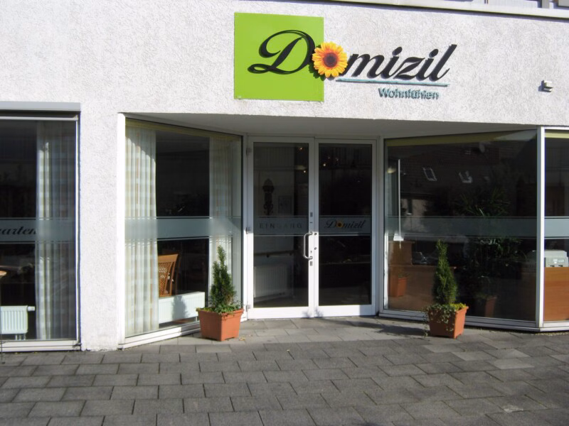 Domizil Velbert Eingangsbereich des Domizil Wohnfühlen mit Glasfront, Beschilderung und bepflanzten Blumenkübeln.